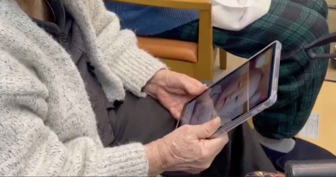 高齢の人が、両手でタブレットを持って画面を見ている手元の写真