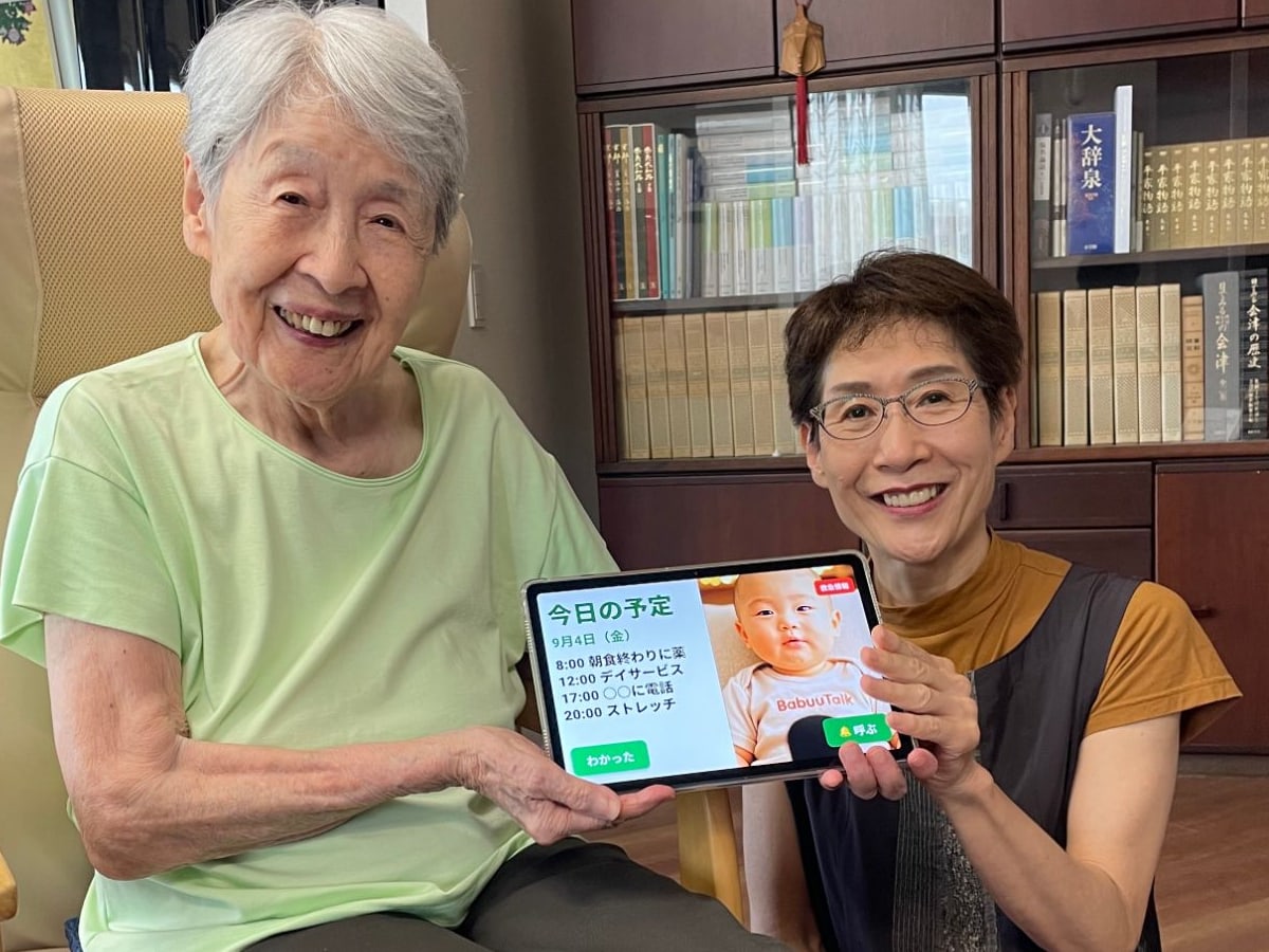 お母様とご家族が並んで、BabuuTalkの画面を映したタブレットを一緒に持っているところ